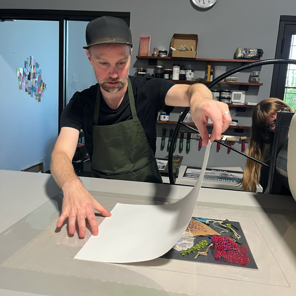 a young man prepares a monoprint to go through the press
